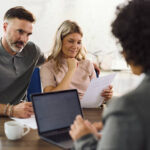 Mid adult couple talking to their bank manager while going through the contract during a meeting in the office. Focus is on woman.