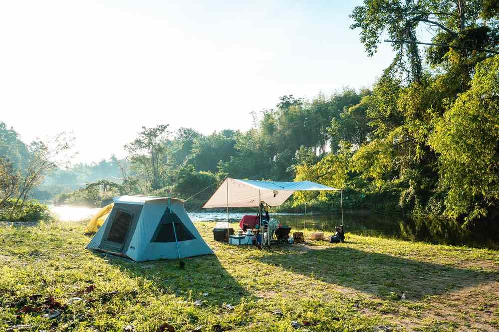Campement avec tente bleue et auvent sous arbres, prairie ensoleillée Campement avec tente bleue et auvent sous arbres, prairie ensoleillée